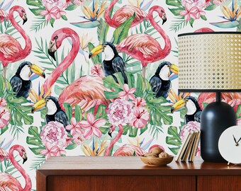 May include: A tropical wallpaper featuring pink flamingos, toucans, and lush green foliage with pink flowers. The wallpaper is displayed on a wooden dresser with a lamp and a bowl of nuts.