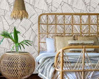 May include: A rattan bed frame with a white and black patterned blanket and a woven headboard. The bed is in front of a white wall with a brown and white banana leaf pattern wallpaper.