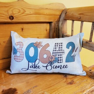 May include: A white pillow with a brown, blue, and white checkered design. The pillow has the numbers 30642 and the text "Lake Conroe" printed on it.