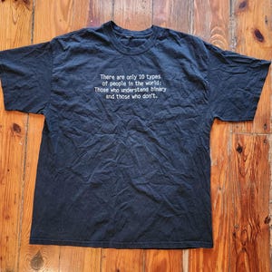 May include: A black t-shirt with white text that reads: "There are only 10 types of people in the world: Those who understand binary and those who don't."