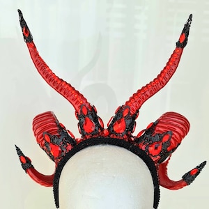 May include: Red devil horn headband with black lace and red rhinestones. The headband is worn on a mannequin head.