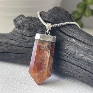 May include: A silver chain necklace with a brown and orange crystal pendant. The pendant is a faceted point with a silver setting.
