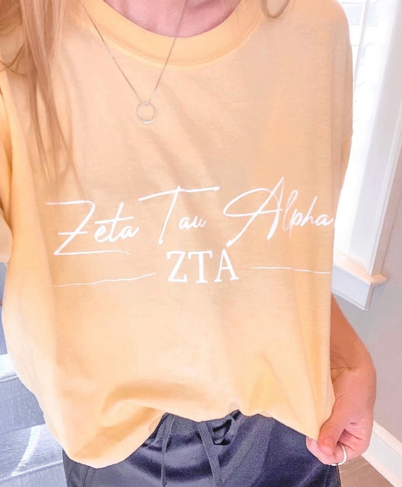 May include: A yellow t-shirt with white text that reads "Zeta Tau Alpha" and "ZTA".