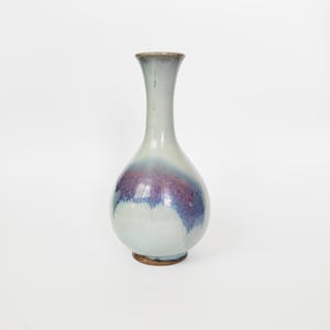 Könnte beinhalten: Eine Keramikvase mit bauchigem Unterteil und einem schlanken, ausgestellten Hals. Die Oberfläche ist mit einer glänzenden Glasur in blassem Grau und Weiß überzogen, die in der Mitte in ein markantes, gesprenkeltes Band aus Violett und Blau übergeht.