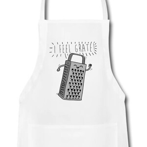 Pu&ograve; includere: Grembiule da cucina bianco con un'illustrazione grigia e bianca di una grattugia con un viso sorridente e il testo "I feel grate".