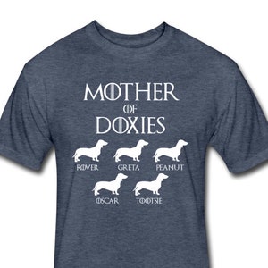 May include: A navy blue t-shirt with the text "Mother of Doxies" in white. Below the text are five white silhouettes of Dachshunds with the names "Rover", "Greta", "Peanut", "Oscar", and "Tootsie" underneath each silhouette.