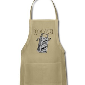 Pu&ograve; includere: Un grembiule da cucina beige con una tasca presenta un'illustrazione di un grattugia con un viso sorridente e il testo "I feel grate".