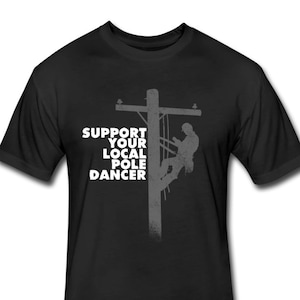 Puede incluir: Camiseta negra con la silueta de una persona subiendo a un poste de electricidad. El texto "SUPPORT YOUR LOCAL POLE DANCER" est&aacute; impreso en blanco en la camiseta.