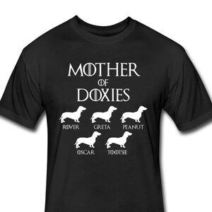May include: Black t-shirt with white text that reads "Mother of Doxies" and features a line of five dachshund silhouettes with names below each: Rover, Greta, Peanut, Oscar, and Tootsie.