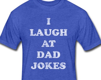 May include: A blue t-shirt with the text "I LAUGH AT DAD JOKES" in white, distressed-style lettering. The shirt has short sleeves and a crew neck. The fabric has a heathered texture.