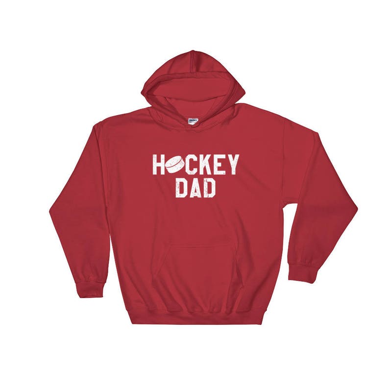 Peut inclure: Sweat-shirt &agrave; capuche rouge avec le texte "HOCKEY DAD" en blanc avec un graphique de rondelle de hockey blanc au-dessus du texte.