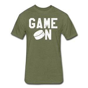 May include: A green t-shirt with the words "GAME ON" in white text. A white hockey puck is above the word "ON".