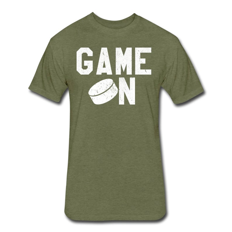 May include: A green t-shirt with the words "GAME ON" in white text. A white hockey puck is above the word "ON".