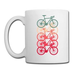 May include: White ceramic mug with a graphic of five bicycles stacked on top of each other. The bicycles are in shades of green, orange, and red.