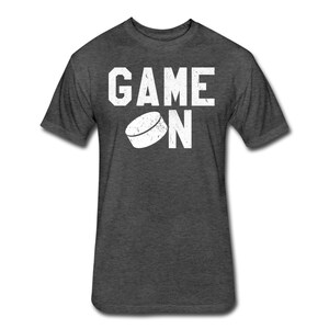 May include: A dark heather grey t-shirt with a white graphic of a hockey puck and the text "GAME ON".
