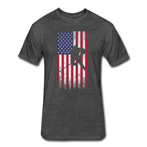 May include: A dark heather grey t-shirt with a distressed American flag design and a silhouette of a hockey player skating. The flag is red, white, and blue.