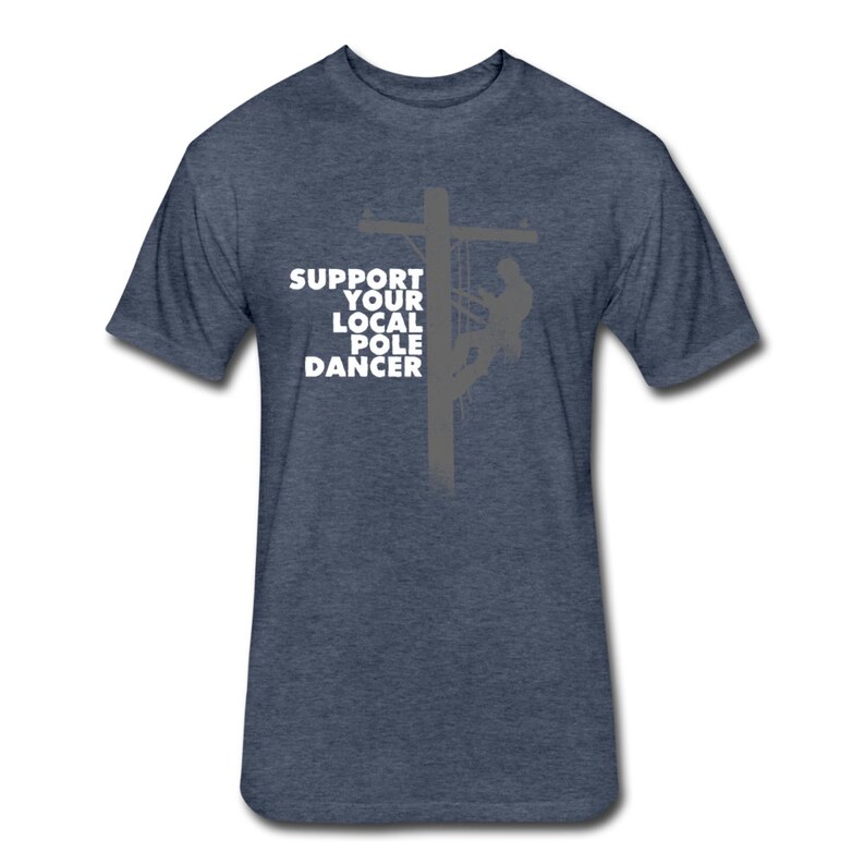 Puede incluir: Una camiseta azul oscuro con un gr&aacute;fico blanco de una silueta de una persona escalando un poste de electricidad. El texto "Support Your Local Pole Dancer" est&aacute; impreso en la camiseta.