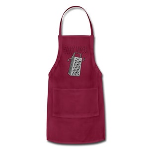 Pu&ograve; includere: Un grembiule da cucina color bordeaux con una tasca che presenta un'illustrazione di un grattugia sorridente con il testo "I feel grate".
