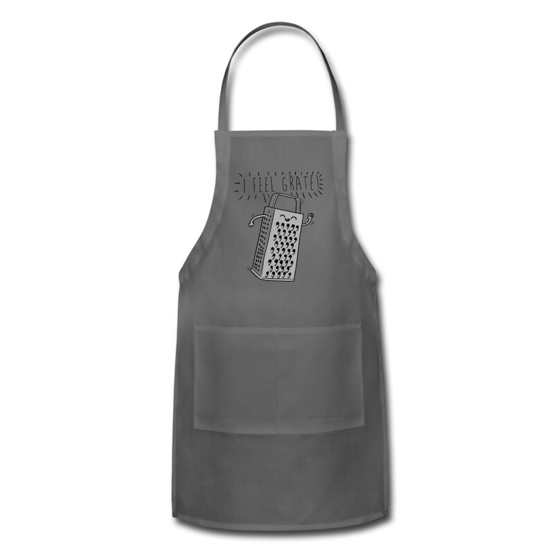 Pu&ograve; includere: Un grembiule grigio con una tasca presenta un'illustrazione in bianco e nero di una grattugia con un viso sorridente e il testo "I feel grate-ful".