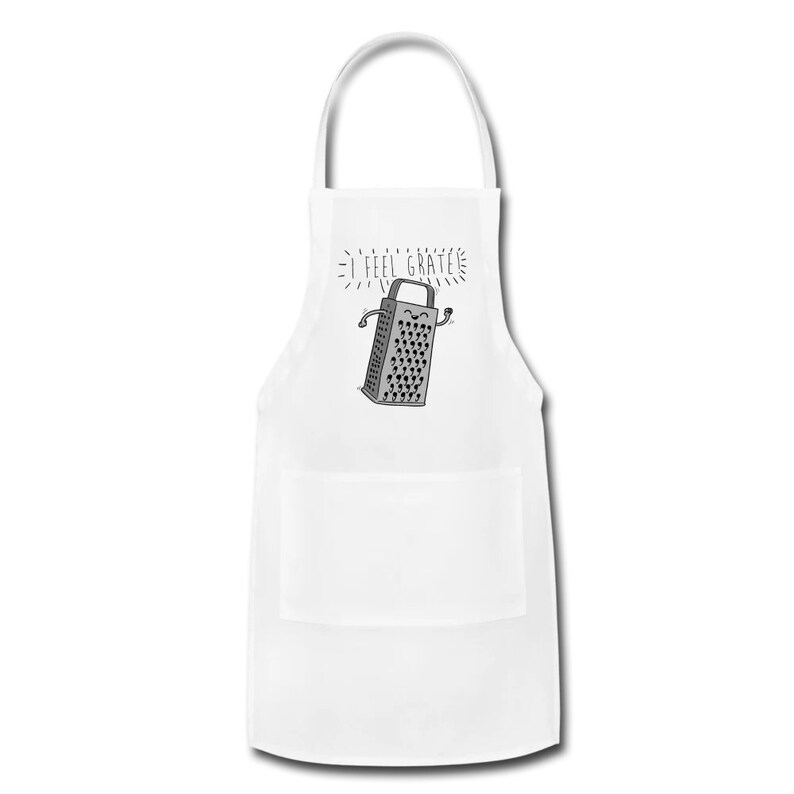 Pu&ograve; includere: Grembiule da cucina bianco con un'illustrazione grigia e bianca di una grattugia con un viso sorridente e il testo "I feel grate".