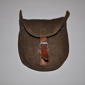 Puede incluir: Una bolsa de lona marrón con una correa de cuero y una hebilla plateada. La bolsa tiene una solapa que se cierra con una hebilla.