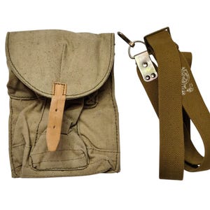 Puede incluir: Una bolsa de lona color beige con cierre de solapa y correa de cuero. La bolsa tiene una correa para el hombro a juego de color beige con un cierre de metal. La bolsa es probablemente de estilo vintage o militar.