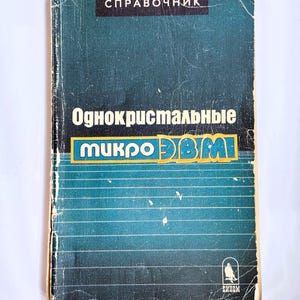 May include: A vintage book with a teal cover and white text. The title includes the words "Справочник" and "Однокристальные микро ЭВМ". The book has a worn appearance, with visible creases and wear along the edges, suggesting age and use. The bottom right corner features a logo.