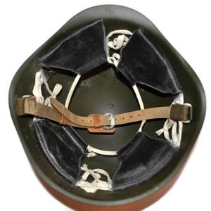 May include: An olive green military helmet, viewed from the inside. The helmet features a brown leather chin strap with a metal buckle and black leather padding. White string is used to secure the padding.
