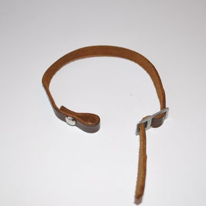 以下が含まれることがあります： 金属製のバックルとスナップ留め具が付いた茶色の革製のストラップ。ストラップはカメラストラップとして使用するために設計されています。