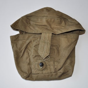 May include: A green canvas canteen cover with a flap and a button closure. The cover has a strap with a buckle.