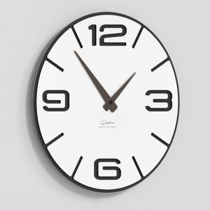 Può includere: Un orologio da parete moderno e rotondo con quadrante bianco e bordo nero. L'orologio presenta grandi numeri neri alle 3, 6, 9 e 12, con linee nere che segnano le altre ore. Le lancette sono marrone scuro. Il testo "MADE IN ITALY" è visibile.