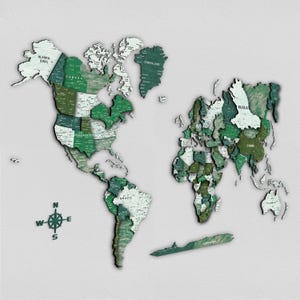 Op de afbeelding: Een houten wereldkaart met 3D-effect, in tinten groen en wit. De kaart toont landnamen en een kompasroos. De continenten zijn gescheiden, wat een gelaagd effect creëert. De kaart is gemonteerd op een lichtgrijze achtergrond.