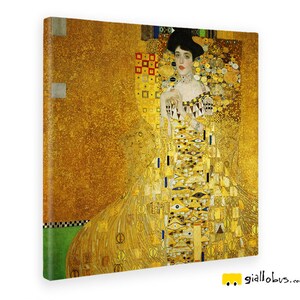 Op de afbeelding: Een schilderij van een vrouw in een gouden jurk met een geometrisch patroon. De achtergrond is ook goudkleurig met een geometrisch patroon. De vrouw draagt een ketting en heeft donker haar.