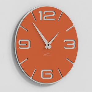 Può includere: Orologio da parete moderno arancione e bianco. Il quadrante è arancione con numeri bianchi intagliati a 3, 6, 9 e 12. Le lancette sono bianche. Prodotto in Italia. Diametro di circa 30 cm.