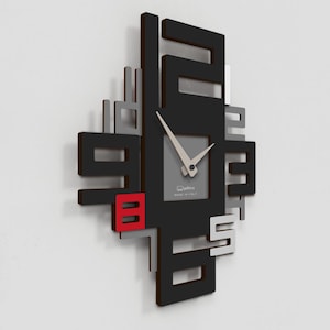 Peut inclure: Horloge murale moderne au design géométrique. L'horloge présente un carré noir avec des formes découpées, des accents gris et blancs, et un accent rouge pour le chiffre 8. Les aiguilles sont argentées et le cadran est gris.