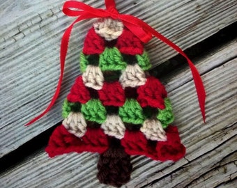 May include: A crocheted Christmas tree ornament in red, green, and cream with a brown yarn trunk. The ornament is attached to a red ribbon with a bow.