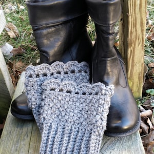 Könnte beinhalten: Ein Paar schwarze Lederstiefel mit grauen Häkel-Stiefelmanschetten. Die Stiefel stehen auf einer Holzoberfläche.