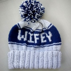 Peut inclure: Un bonnet en tricot blanc et bleu avec un pompon sur le dessus. Le bonnet a le mot "WIFEY" tricoté sur le devant.