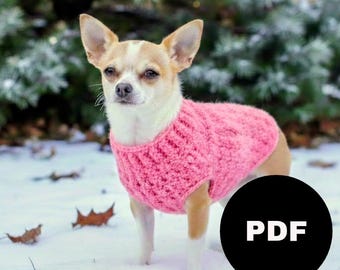 May include: A small dog wearing a pink knitted sweater stands in the snow. The dog has tan and white fur and is looking at the camera. A black circle with the word "PDF" in white is in the lower right corner.
