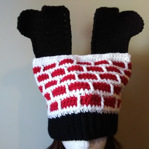 May include: A crocheted hat with a brick pattern in red and white. The hat has two black crocheted legs sticking out of the top.