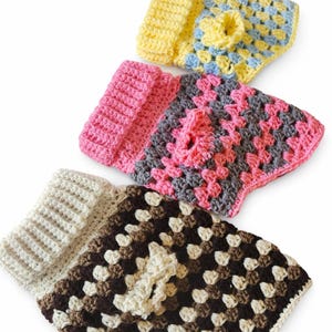 Puede incluir: Tres suéteres para perros tejidos a crochet en varios colores. El suéter superior es amarillo y azul, el del medio es rosa y gris, y el inferior es marrón y crema. Cada suéter tiene un cuello acanalado y un agujero para la correa del perro.