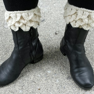 May include: Black ankle boots with white crocheted leg warmers. The leg warmers have a scalloped edge.