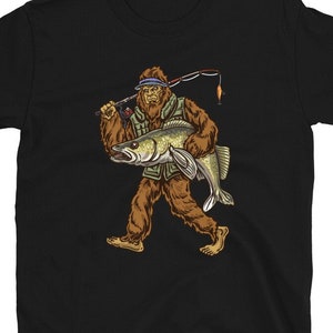 Op de afbeelding: Zwart T-shirt met een afbeelding van een Bigfoot die een vis vasthoudt. De Bigfoot draagt ​​een hoed en houdt een hengel vast.