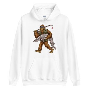 Puede incluir: Sudadera con capucha blanca con un estampado gr&aacute;fico de un personaje de Bigfoot que lleva un sombrero de pesca y sostiene un pez grande.