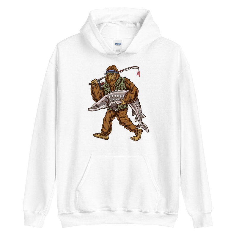 Puede incluir: Sudadera con capucha blanca con un estampado gr&aacute;fico de un personaje de Bigfoot que lleva un sombrero de pesca y sostiene un pez grande.