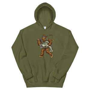 May include: A green hooded sweatshirt with a graphic print of a Bigfoot holding a fish. The Bigfoot is wearing a hat and a vest.