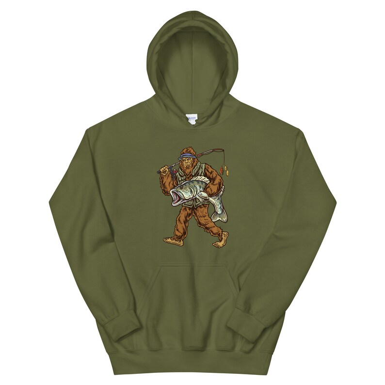 May include: A green hooded sweatshirt with a graphic print of a Bigfoot holding a fish. The Bigfoot is wearing a hat and a vest.