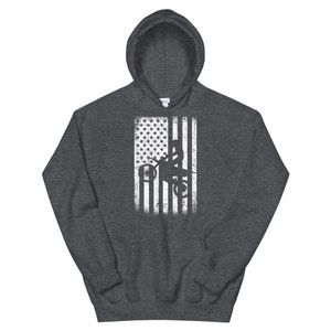 May include: A dark grey hooded sweatshirt with a white distressed American flag design featuring a silhouette of a person riding a dirt bike.