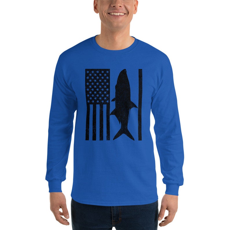 Pu&ograve; includere: Una t-shirt a maniche lunghe blu reale con una silhouette nera di un pesce e una bandiera americana.