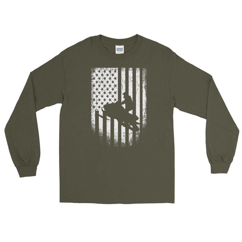 K&ouml;nnte beinhalten: Ein gr&uuml;nes Langarmshirt mit einem wei&szlig;en, abgenutzten amerikanischen Flaggen-Design, das die Silhouette einer Person auf einem Schneemobil zeigt.